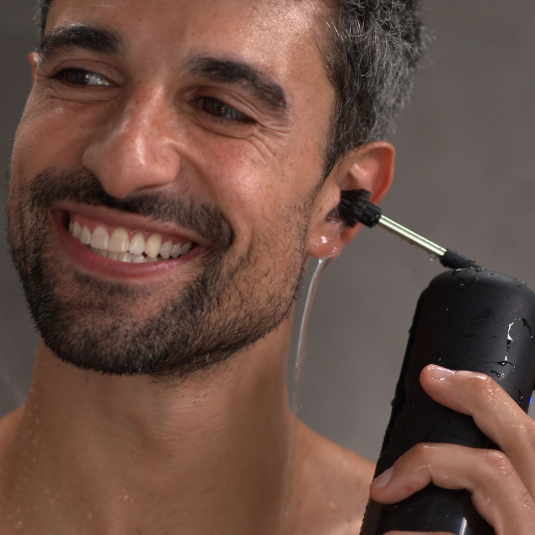 Man smiling while using an ear cleaning device in the shower.