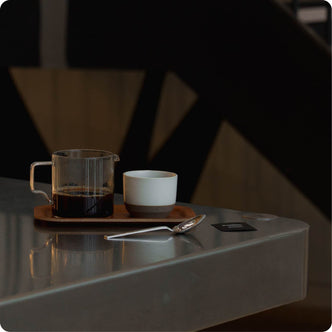 A barista with tattoos pours hot water from a kettle into a pour-over coffee dripper.