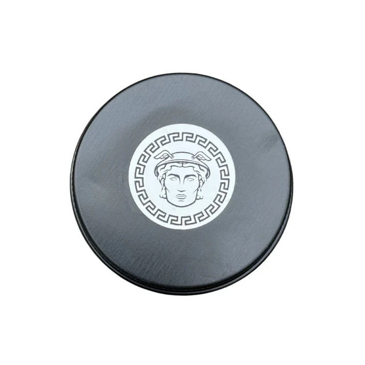 A round, black container lid with a white sticker showing the head of Hermes in a Greek key border.