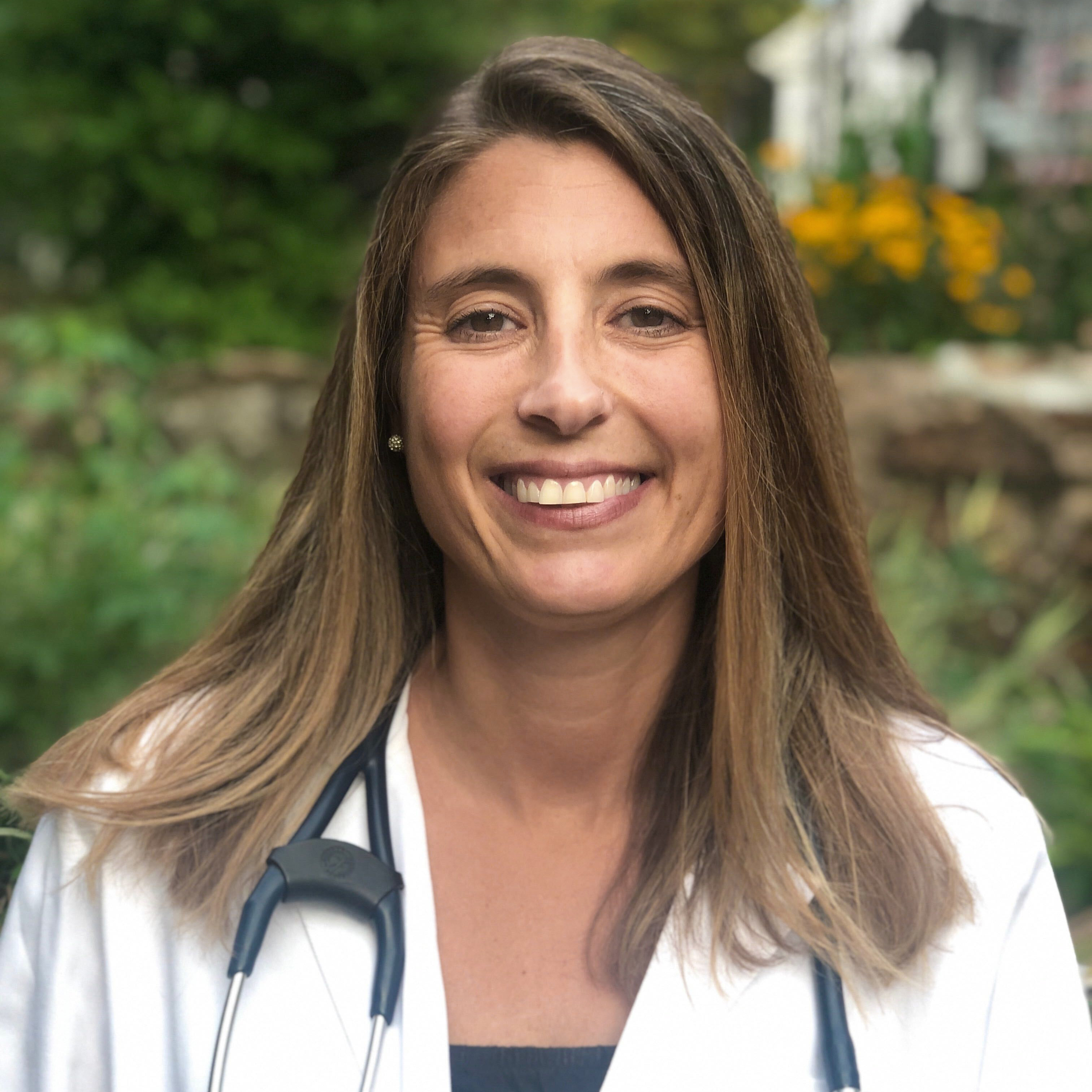 Smiling person with a stethoscope in a garden setting.