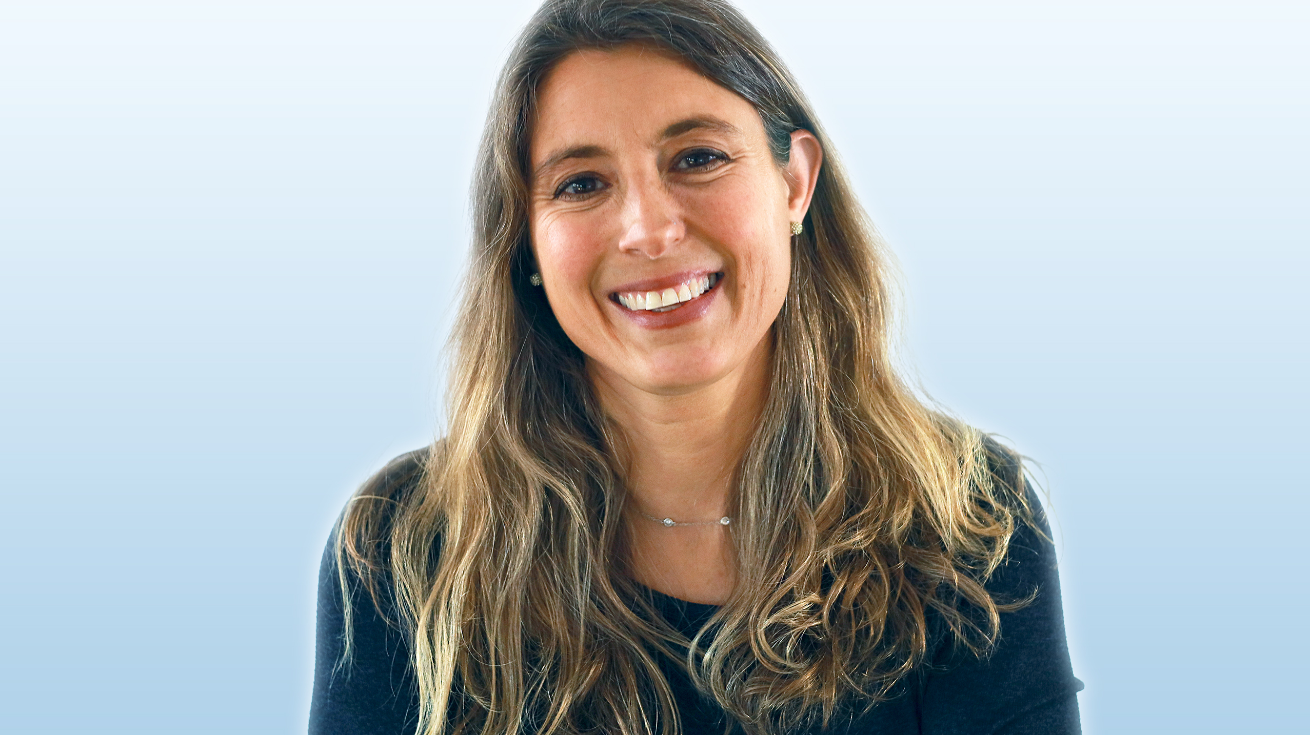 Headshot of a smiling woman with long, light brown hair against a light blue gradient background.