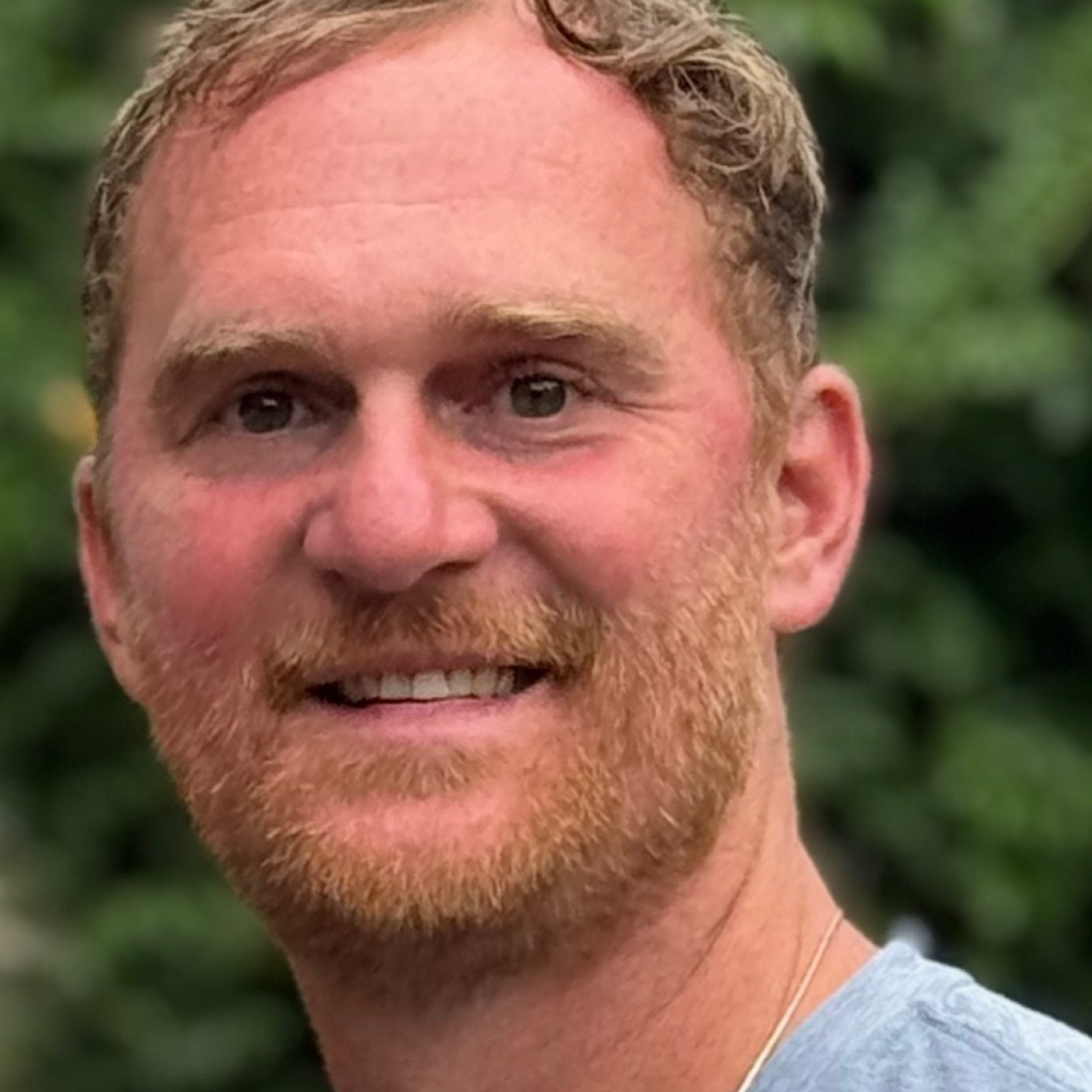 Close-up of a smiling person with short hair and facial hair.