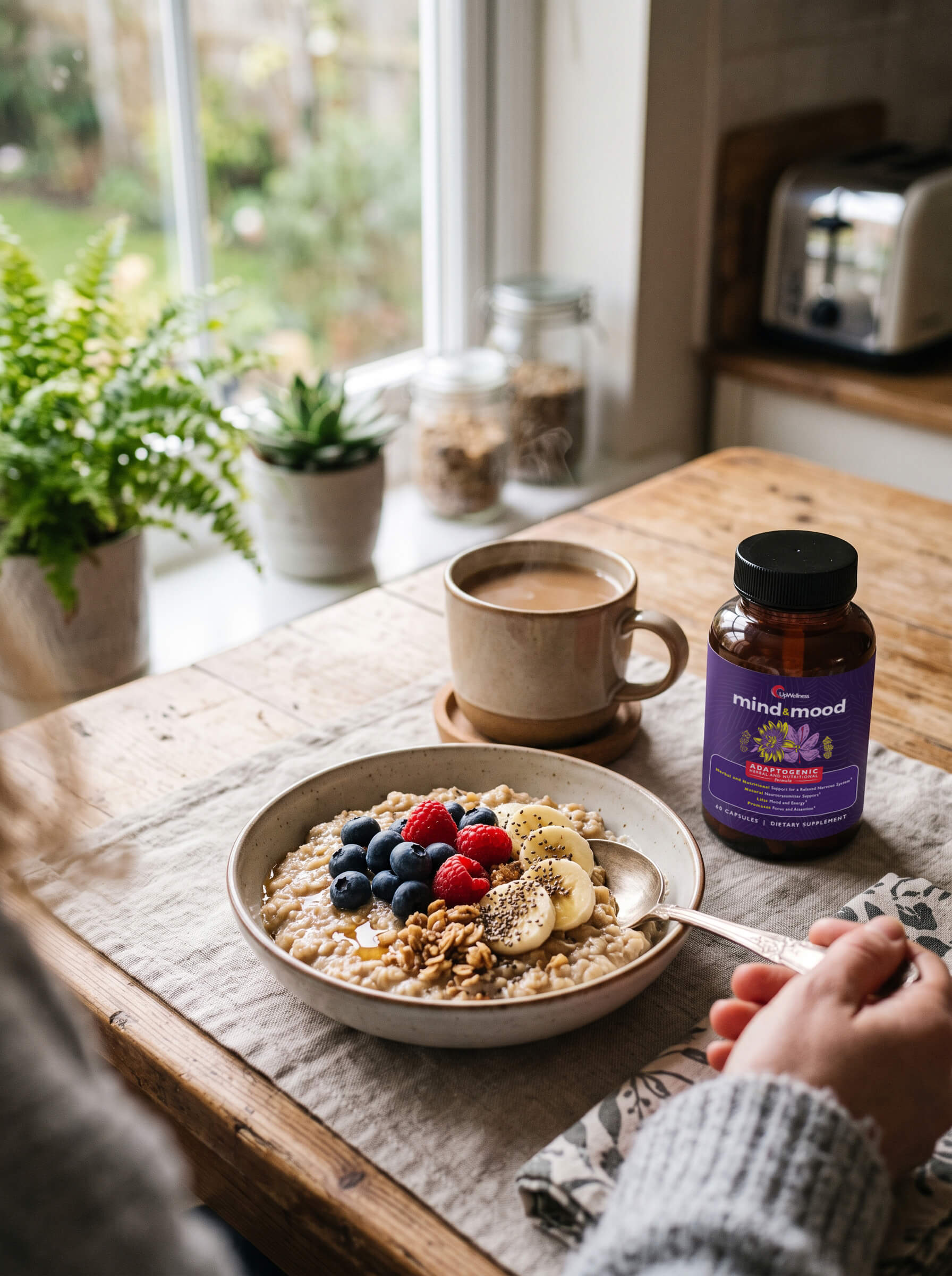 A person eats a bowl of oatmeal with fruit, next to a coffee and a bottle of supplements.