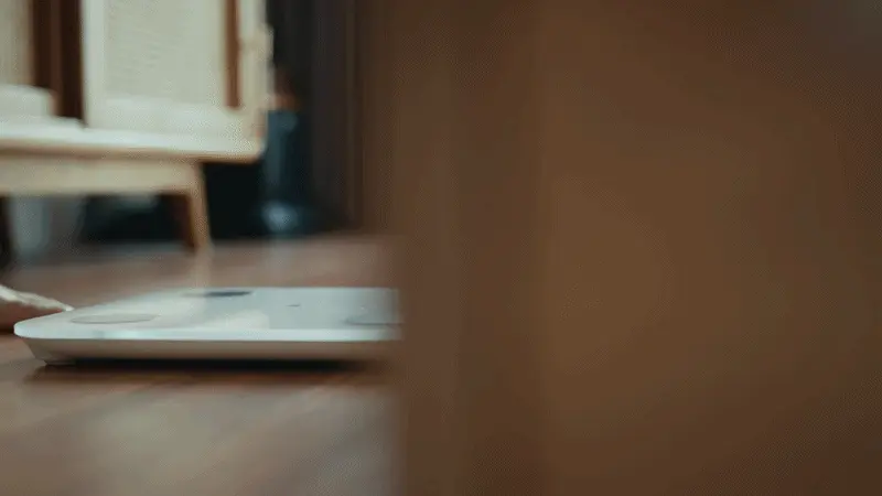 A low-angle shot of a person's feet stepping onto a white digital scale on a wooden floor.