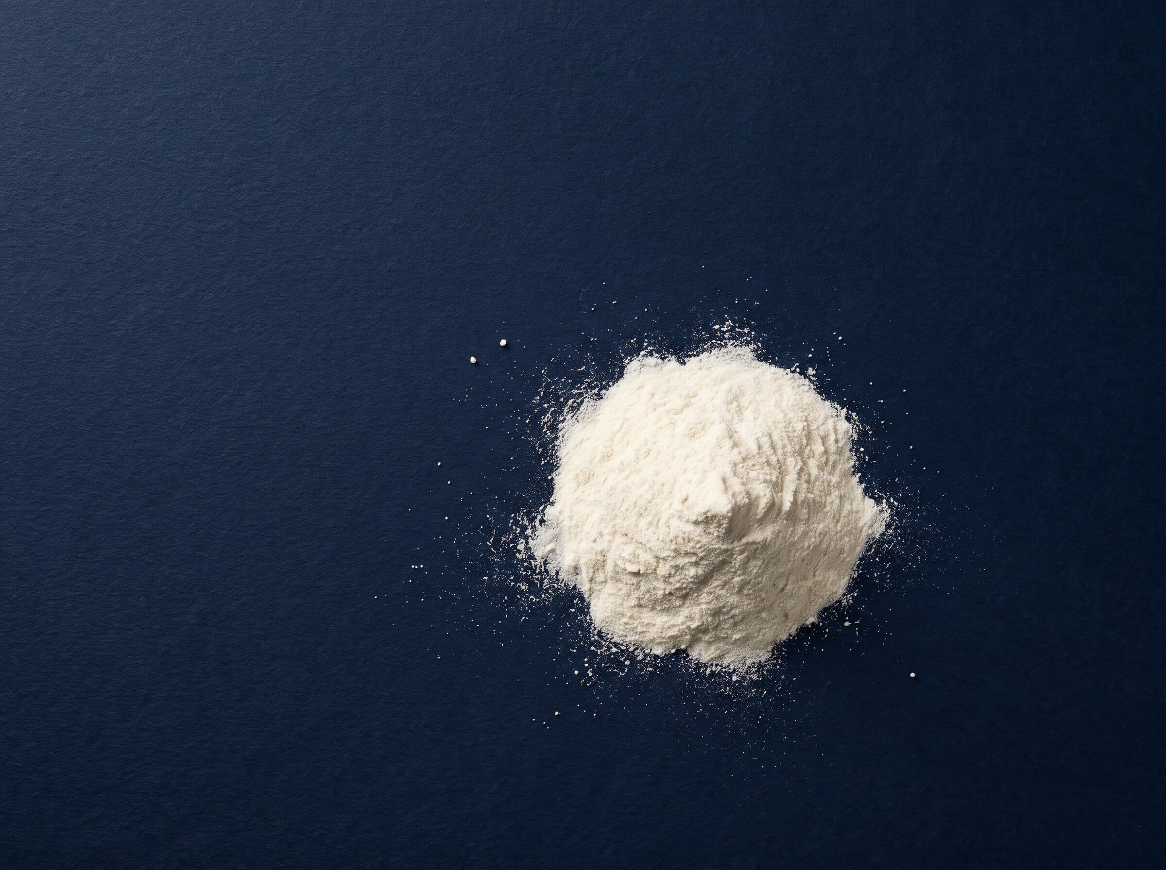 An overhead shot of a small pile of white powder on a dark blue textured background.
