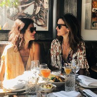 Two women sitting at a restaurant table with food and drinks.