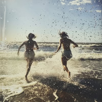 Two people running through ocean waves with water splashing around them.