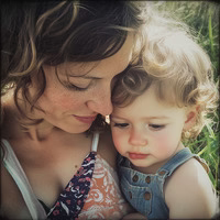 A woman and child with curly hair embracing outdoors.