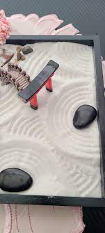 Miniature zen garden with sand, stones, and a small bridge.