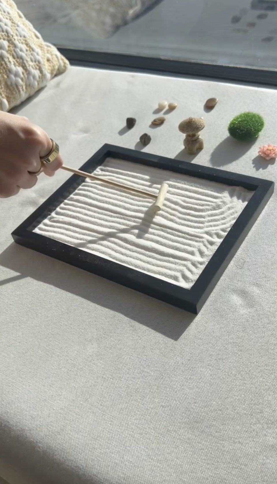 Hand raking patterns in a small tabletop zen garden with sand and stones.