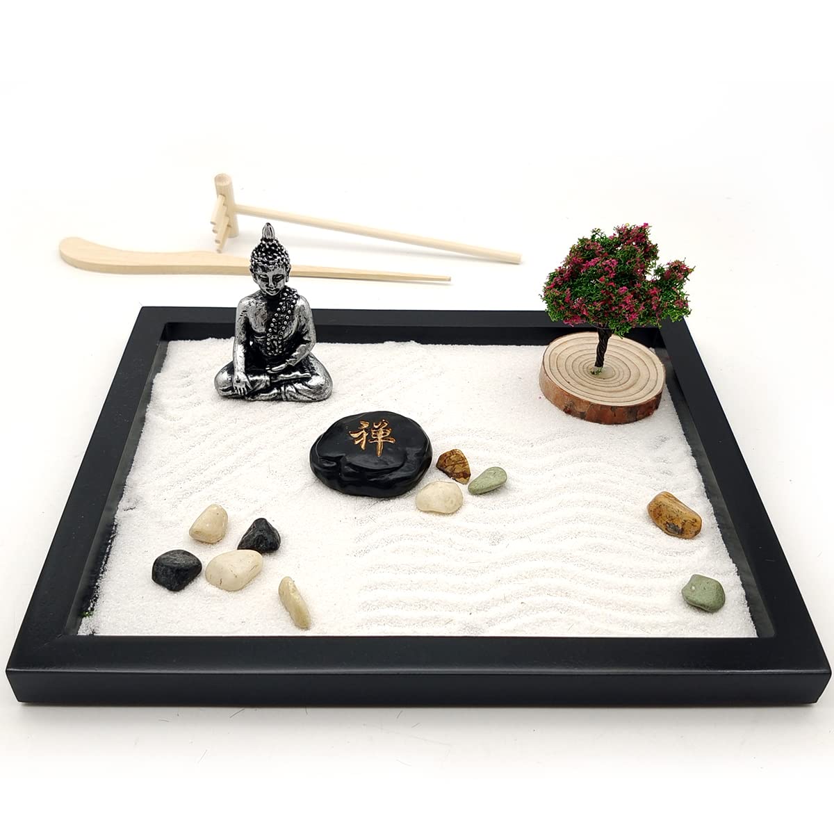 Miniature zen garden with Buddha statue, rocks, and a small tree on white sand.