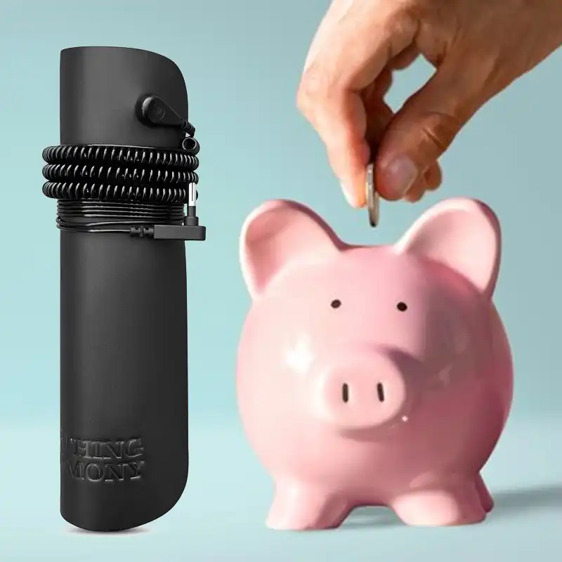Hand placing coin into pink piggy bank beside a black cylindrical object.