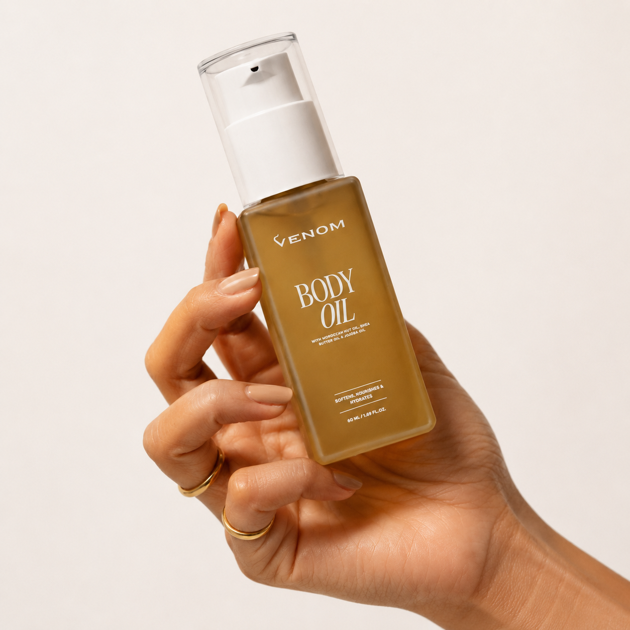 A person's hand with manicured nails holding a bottle of Venom Body Oil against a white background.