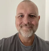 A person with a shaved head and beard smiling at the camera.