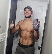 Man taking a mirror selfie, shirtless, wearing a cap and holding a phone.