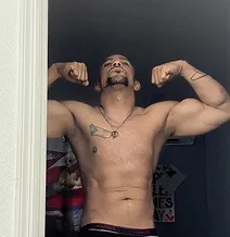 Shirtless man flexing his muscles, standing in a doorway.