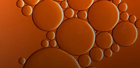 A close-up abstract image of orange-colored oil droplets clustered together.