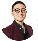 A headshot of a smiling East Asian man with glasses wearing a black shirt and a maroon blazer.