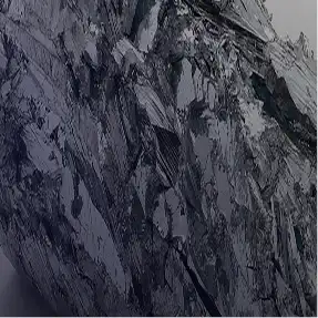 A close-up of a dark, shiny, crystalline mineral with a jagged, layered texture.