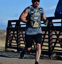 Man in athletic gear running on a paved path near a bridge.