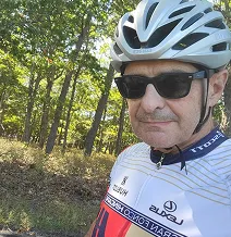Person wearing a cycling helmet and sunglasses, standing outdoors with trees in the background.
