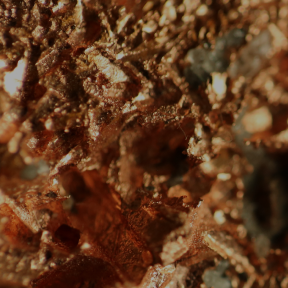 A close-up, macro view of coppery, metallic mineral flakes and dark green crystals.