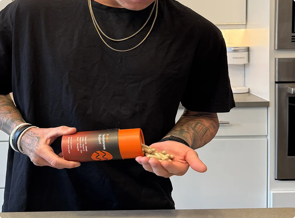 A tattooed person in a black shirt pours capsules from a container into their hand.