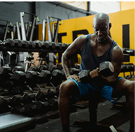 Man lifting dumbbells in a gym with weights in the background.