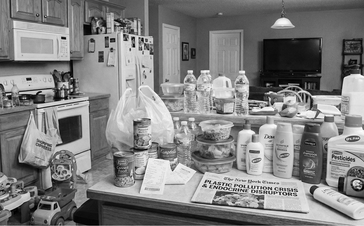 A black and white photo of a cluttered kitchen counter with plastic containers, groceries, and a newspaper.