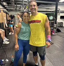 Two people smiling in a gym setting, wearing athletic attire.