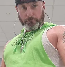 Man wearing green sleeveless hoodie and headphones looks at camera.