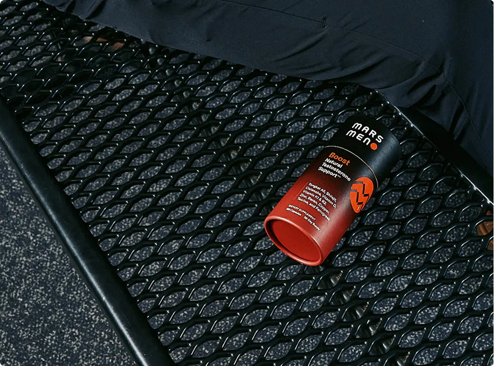 A black and red container of Mars Men Boost supplement lying on a black mesh bench.
