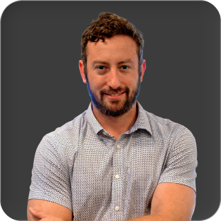 A headshot of a smiling man with a beard, wearing a patterned short-sleeved button-down shirt.
