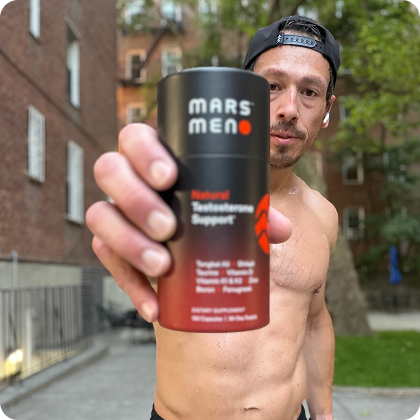 A shirtless man in a baseball cap holds a container of Mars Men testosterone support supplement outdoors.