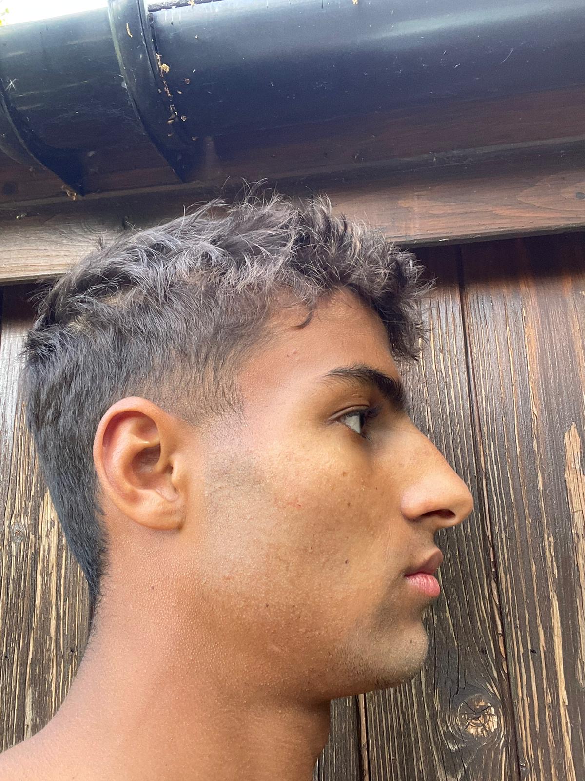 Side profile of a person with short hair against a wooden background.