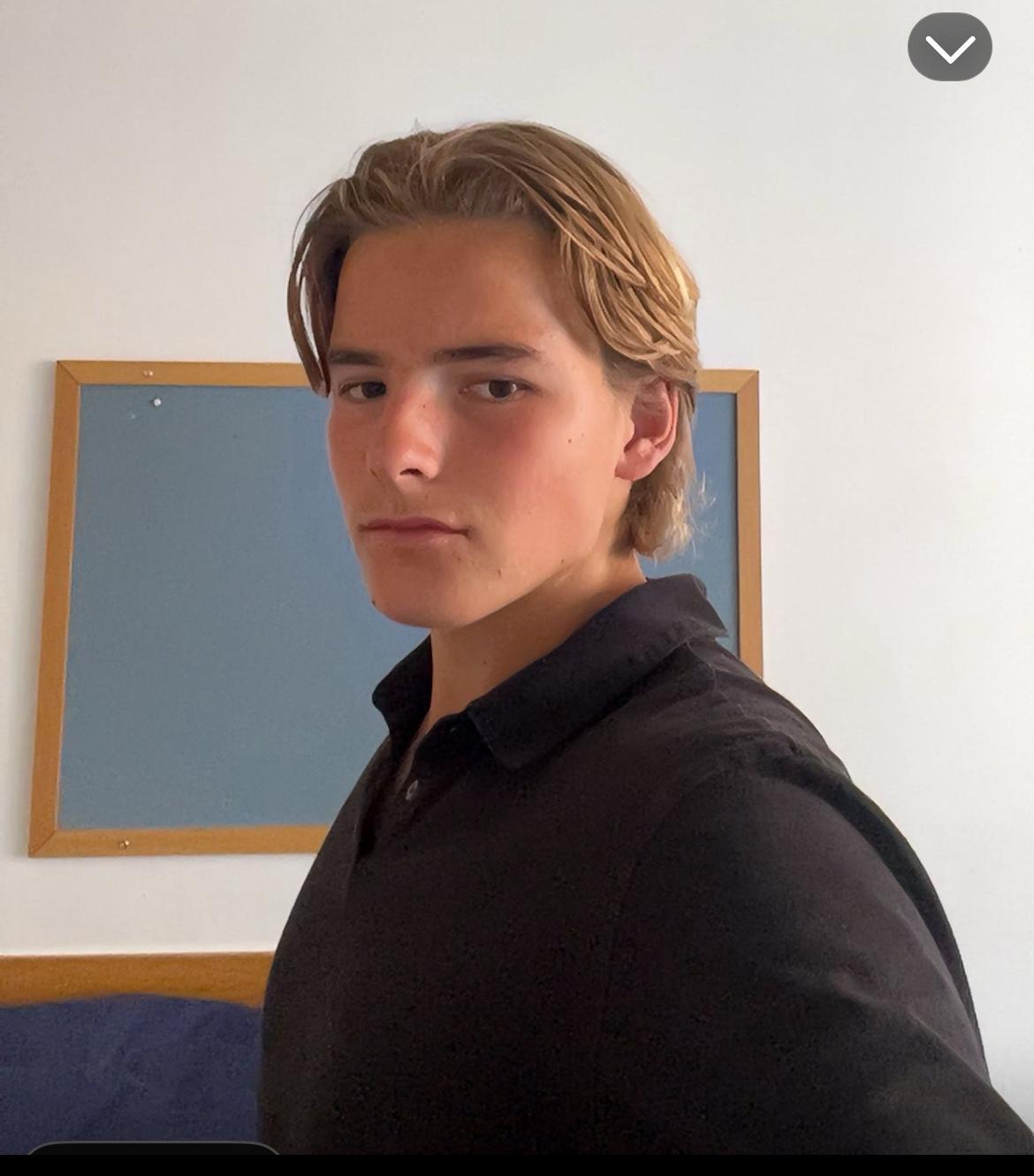 Person with short hair wearing a black shirt, standing indoors.