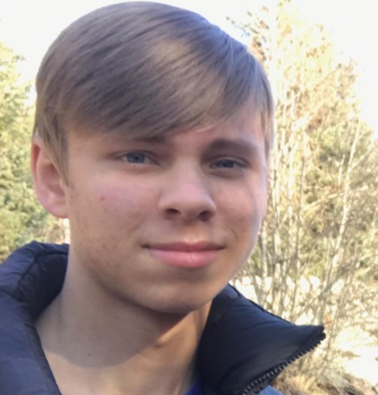 Young person outdoors with trees in the background.