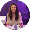 A woman smiling at a table with gadgets and a purple background.