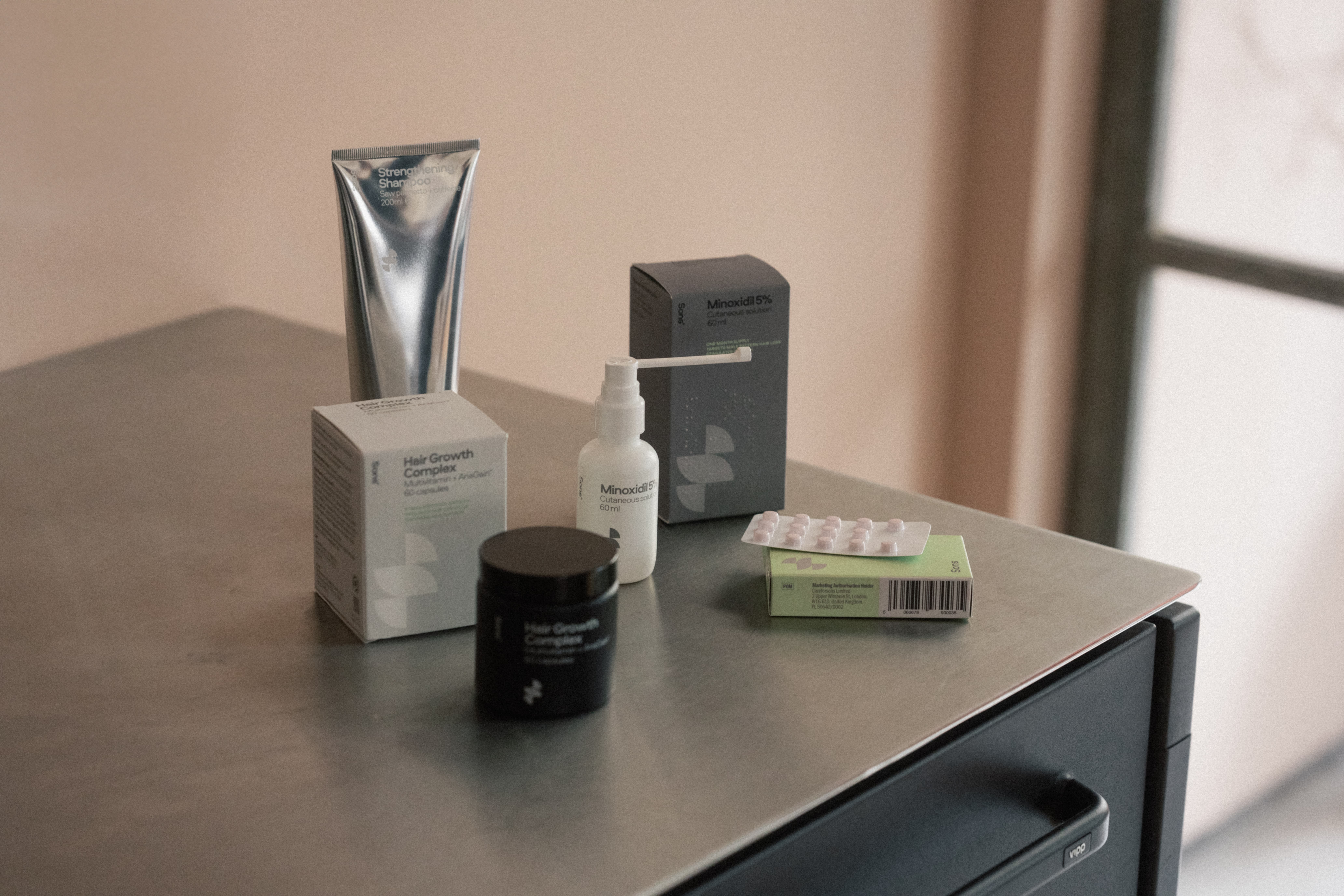 Assorted hair care products on a metal surface, including shampoo, capsules, and a spray bottle.