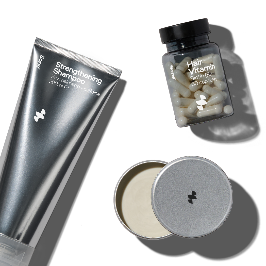 Shampoo tube, hair vitamin bottle, and tin of cream on a white background.