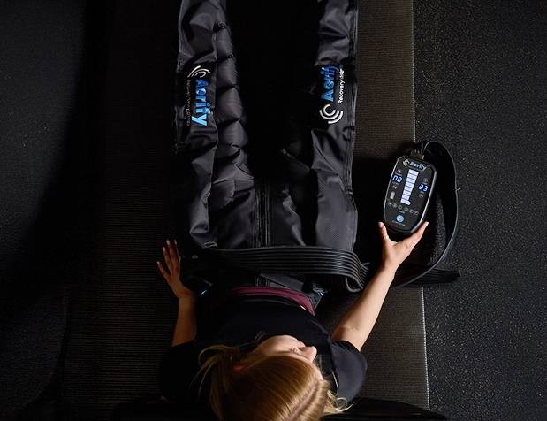 Person using leg compression therapy device with control panel.