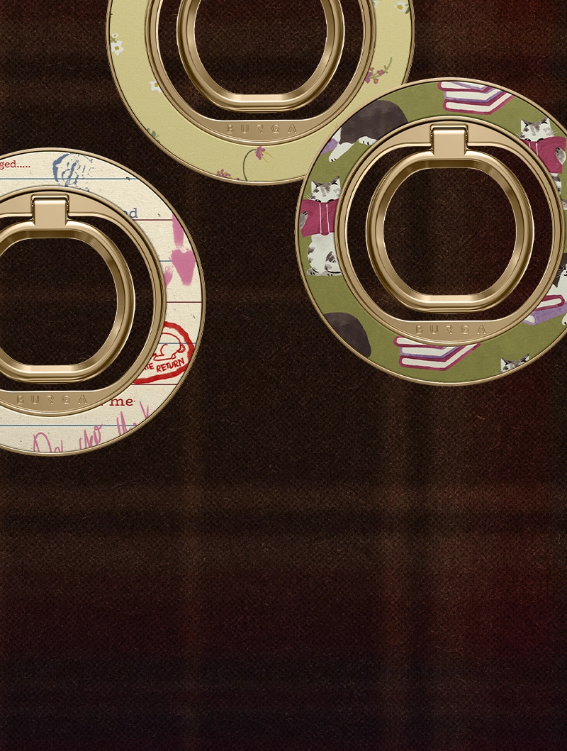 A close-up of three different decorative BURGA phone ring holders on a dark textured background.