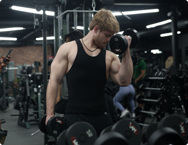 Man lifting dumbbells in a gym, wearing a black tank top.
