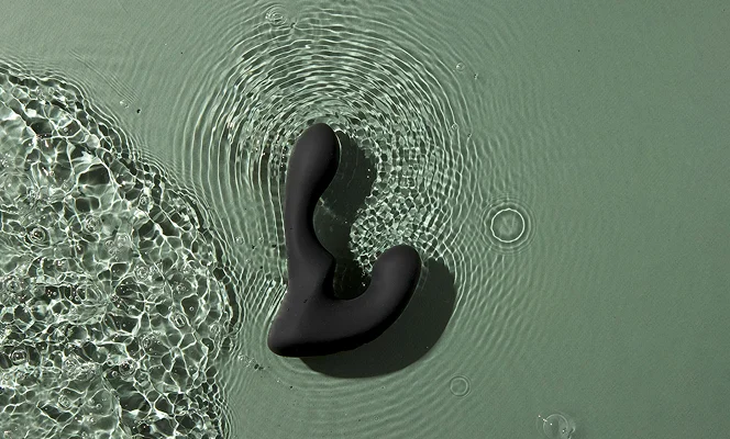 Prostate Massager Giddy Tomo floating in water with ripples on a green background.