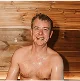 Person sitting in a sauna with wooden walls, smiling.