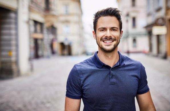Smiling man in a blue shirt standing on a cobblestone street.