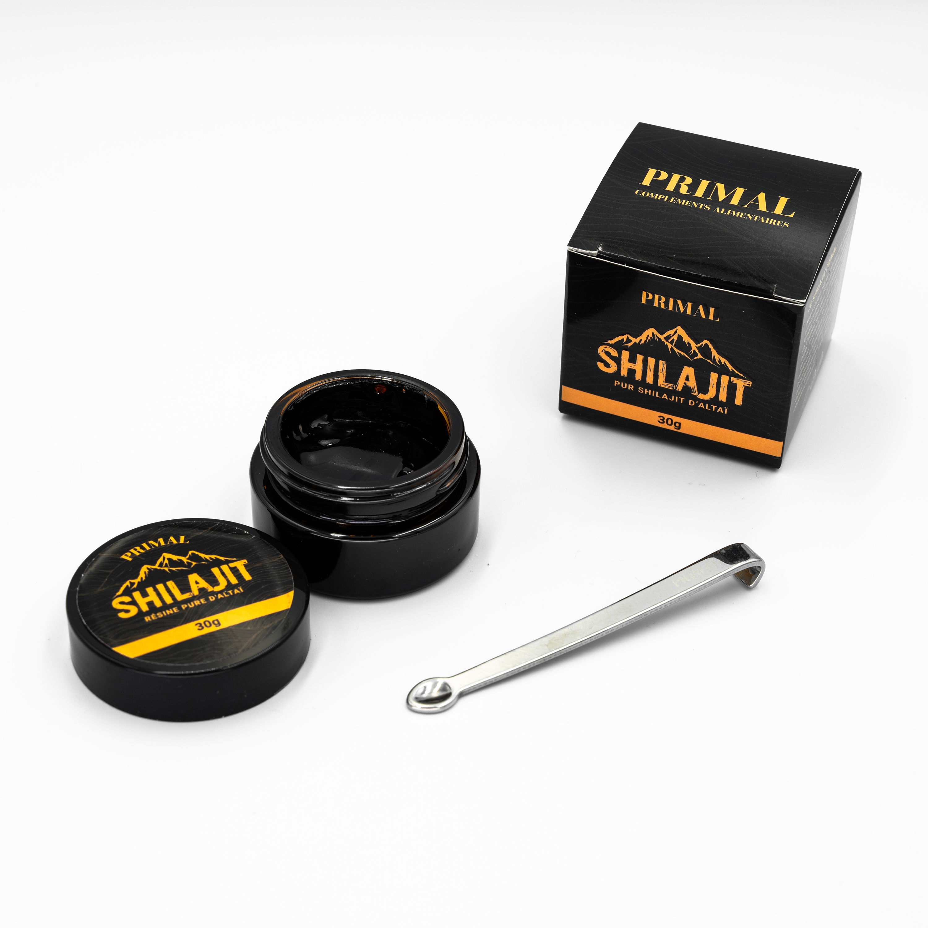 Black jar and box of Shilajit with a metal spoon on white background.