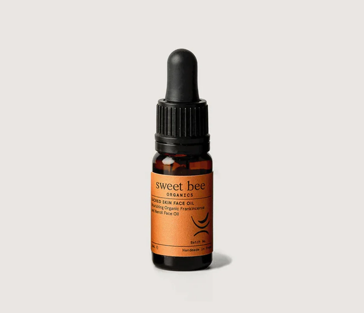A small brown glass dropper bottle of Sweet Bee Organics face oil on a plain, off-white background.