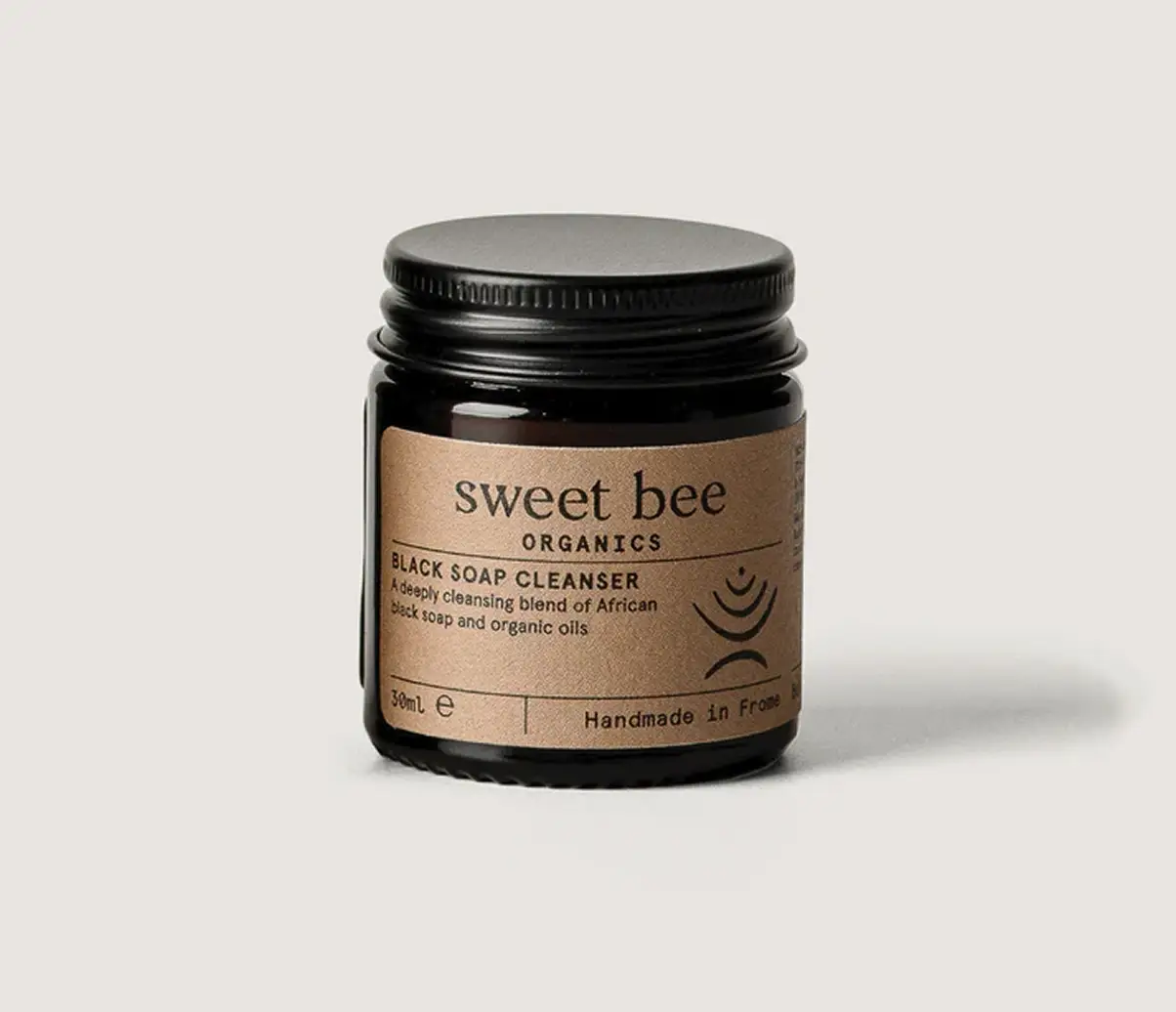 A small amber glass jar of Sweet Bee Organics Black Soap Cleanser on a light grey background.