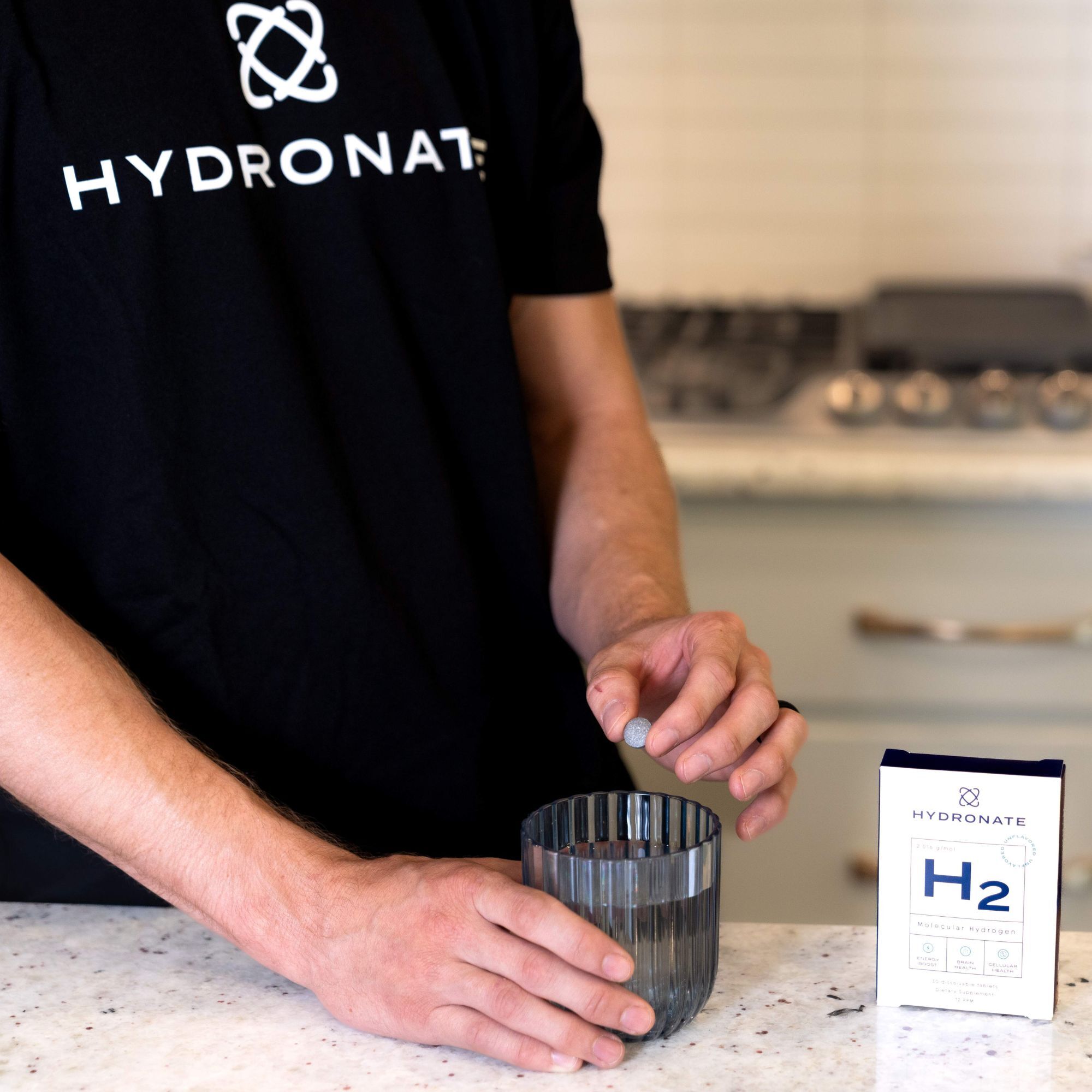 Person dropping a tablet into a glass, next to a box labeled 'Hydronate H2'.